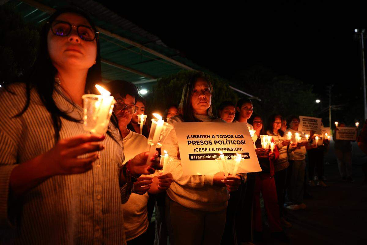 Venezuelan activists at a candlelight vigil holding a sign reading 'Liberen a todos los presos políticos · ¡Cese la represión!'