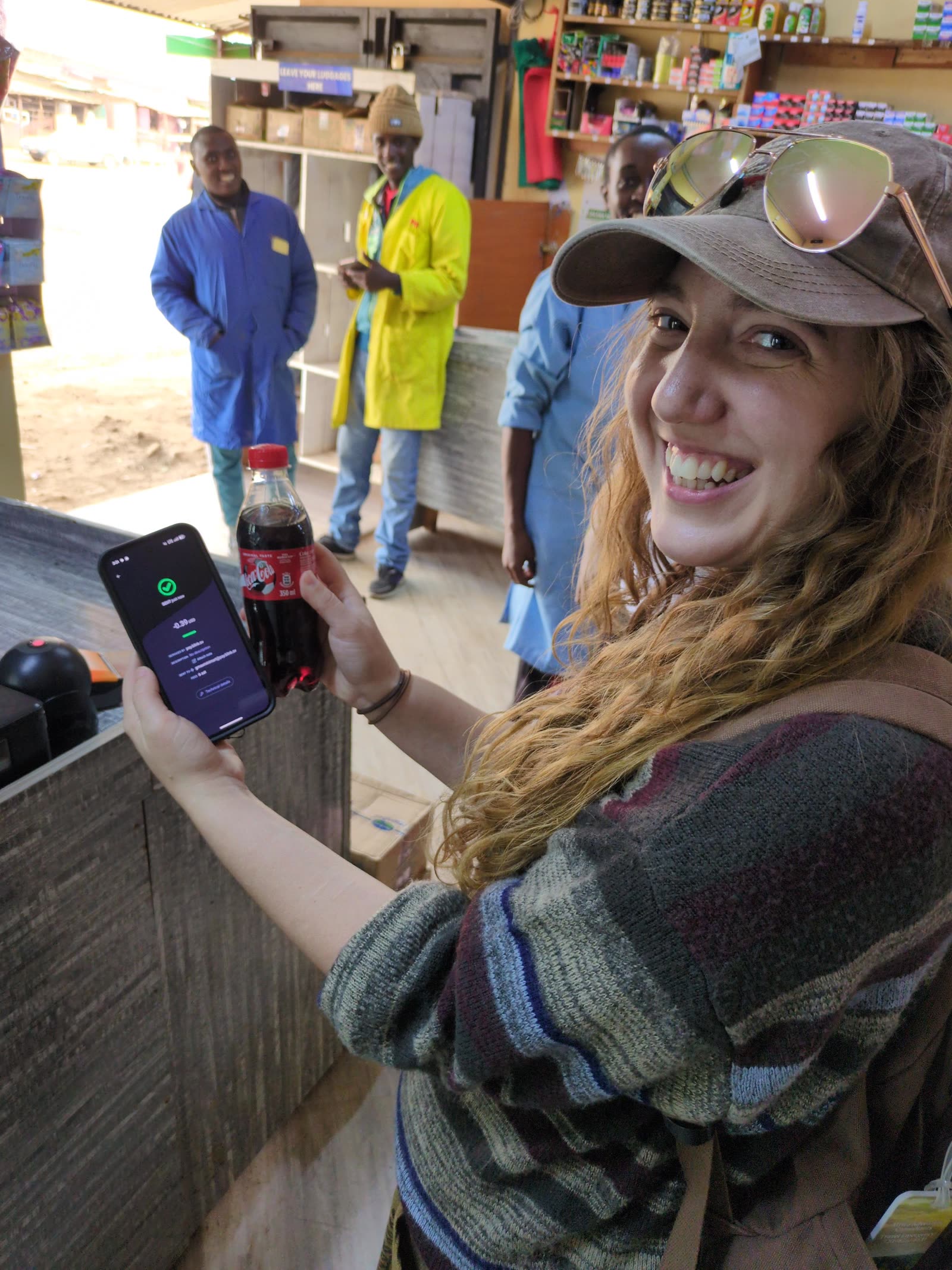 M.K. Fain smiling while paying for a Coca-Cola with a Bitcoin Lightning wallet at a shop in Matangi, Kenya