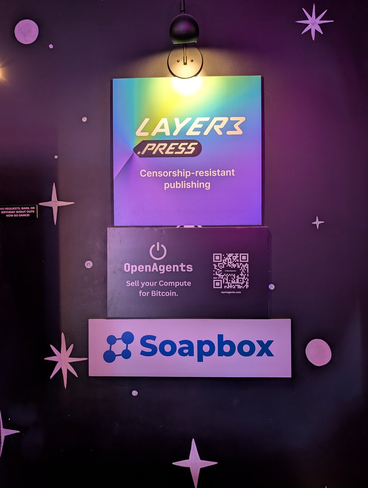 Sponsor wall at NosVegas 2.0 featuring Layer3.press, OpenAgents, and Soapbox logos against the venue's purple-and-stars decor